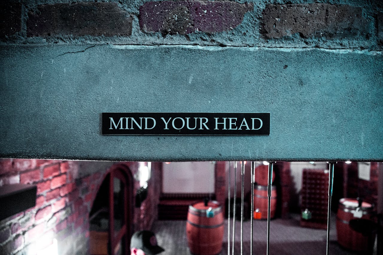 A Mind Your Head sign in a rustic brick barrel cellar setting, creating a safety awareness ambiance.